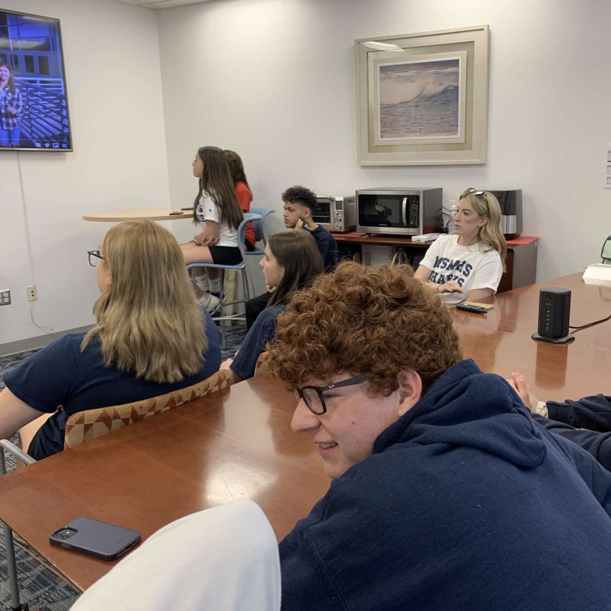 Students watch a TV screen displaying the 2023 lip dub.